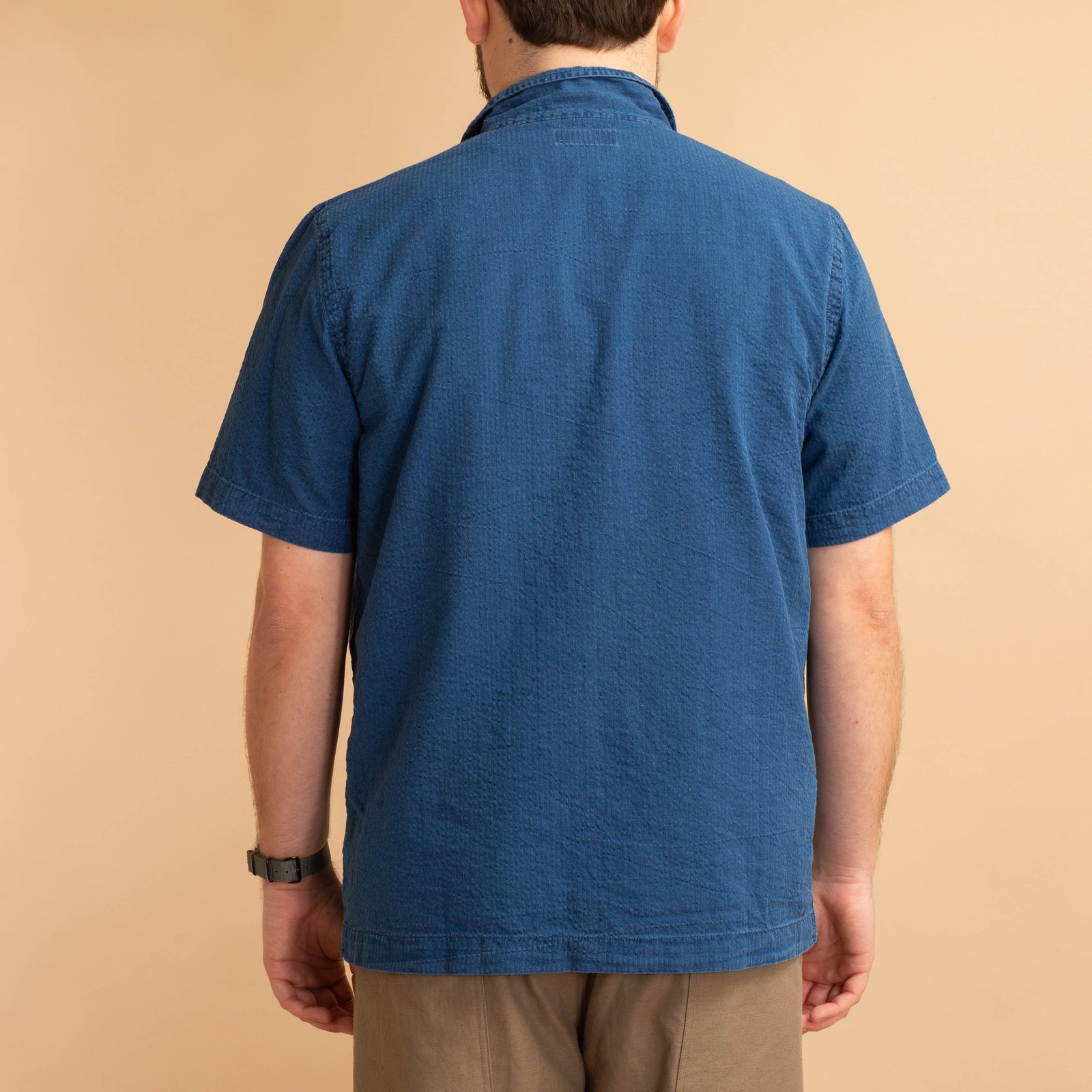 UNIVERSAL WORKS Road Shirt in Washed Indigo Seersucker worn from the back, loafers.