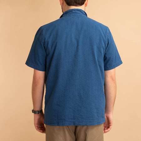 UNIVERSAL WORKS Road Shirt in Washed Indigo Seersucker worn from the back, loafers.